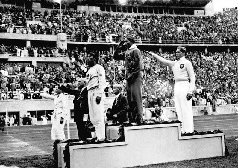 1936 წლის ბერლინის ოლიმპიური თამაშები, სიგრძეზე ხტომაში მედლების დაჯილდოების ცერემონია: ცენტრ ოუენსი (აშშ) პირველი, მარცხნივ: ტაჯიმა (იაპონია) მესამე, მარჯვნივ: ლონგი (გერმანია) მეორე.