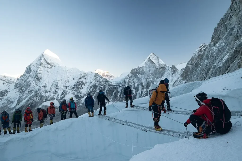 Climbers crossing an aluminum ladder bridge over a deep crevasse in the Khumbu Icefall on Mount Everest.