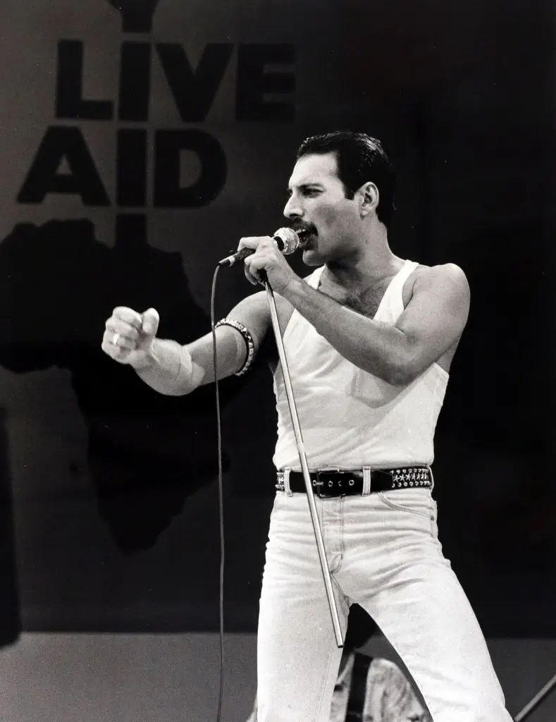 Фредди Меркьюри выступает на Live Aid в белой майке, держа в руке сломанную стойку микрофона.